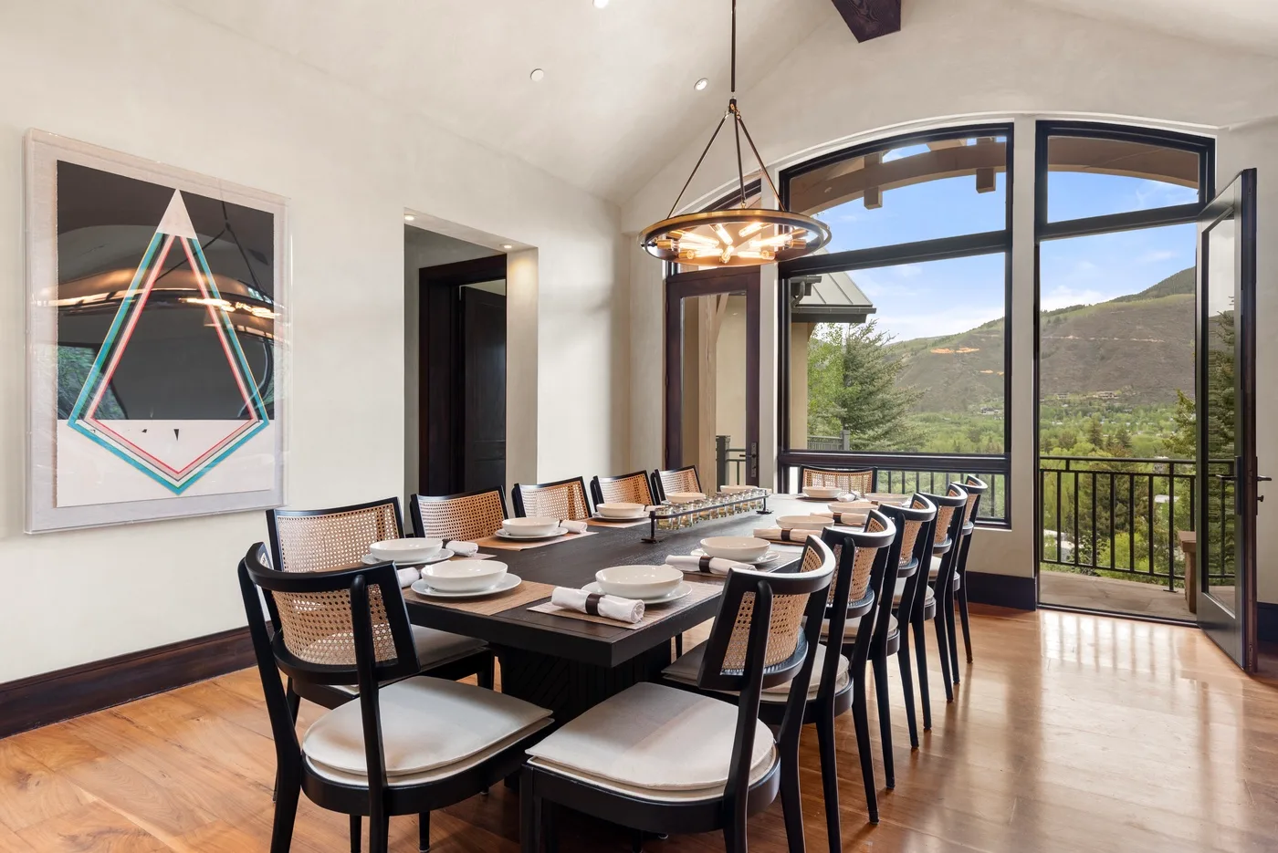 Un comedor con una mesa larga y grandes ventanales con vistas a una ladera verde.