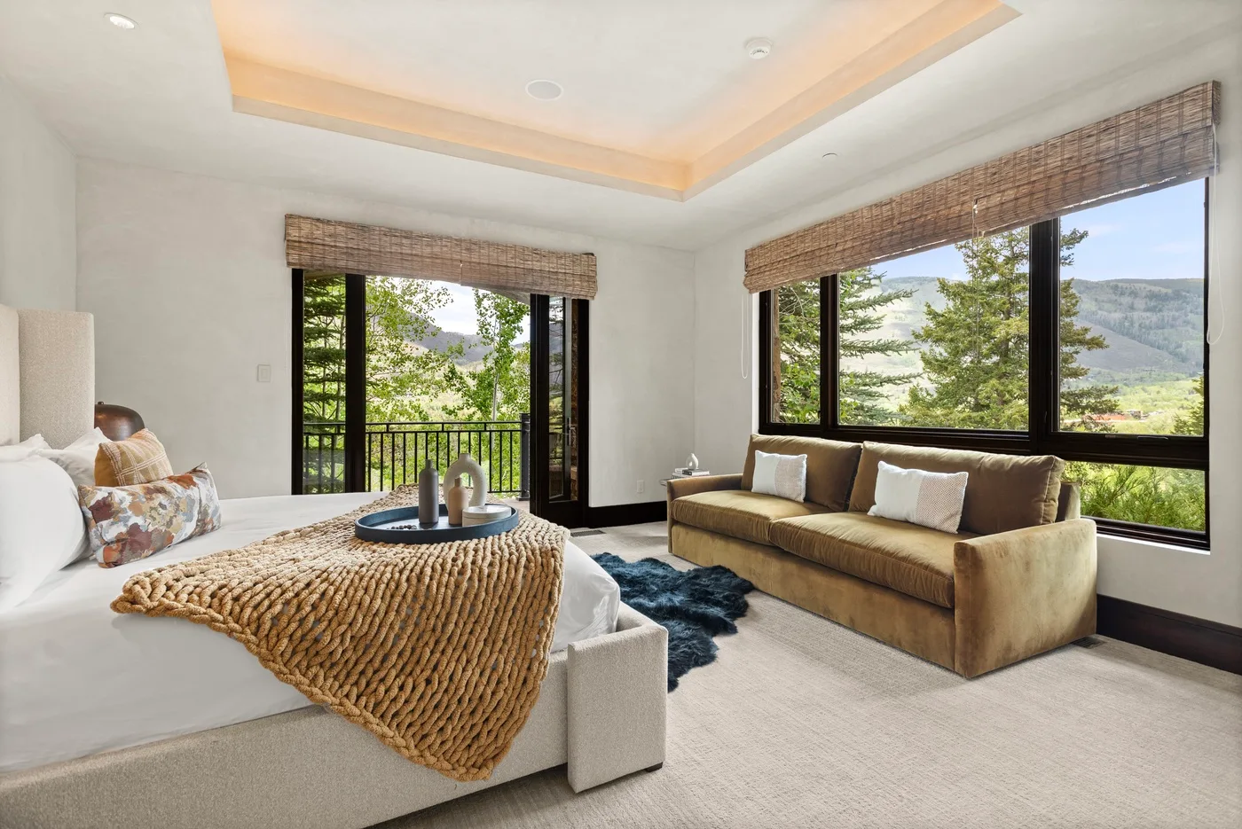 Un dormitorio luminoso con cama, asientos y grandes ventanas con vistas a la vegetación.