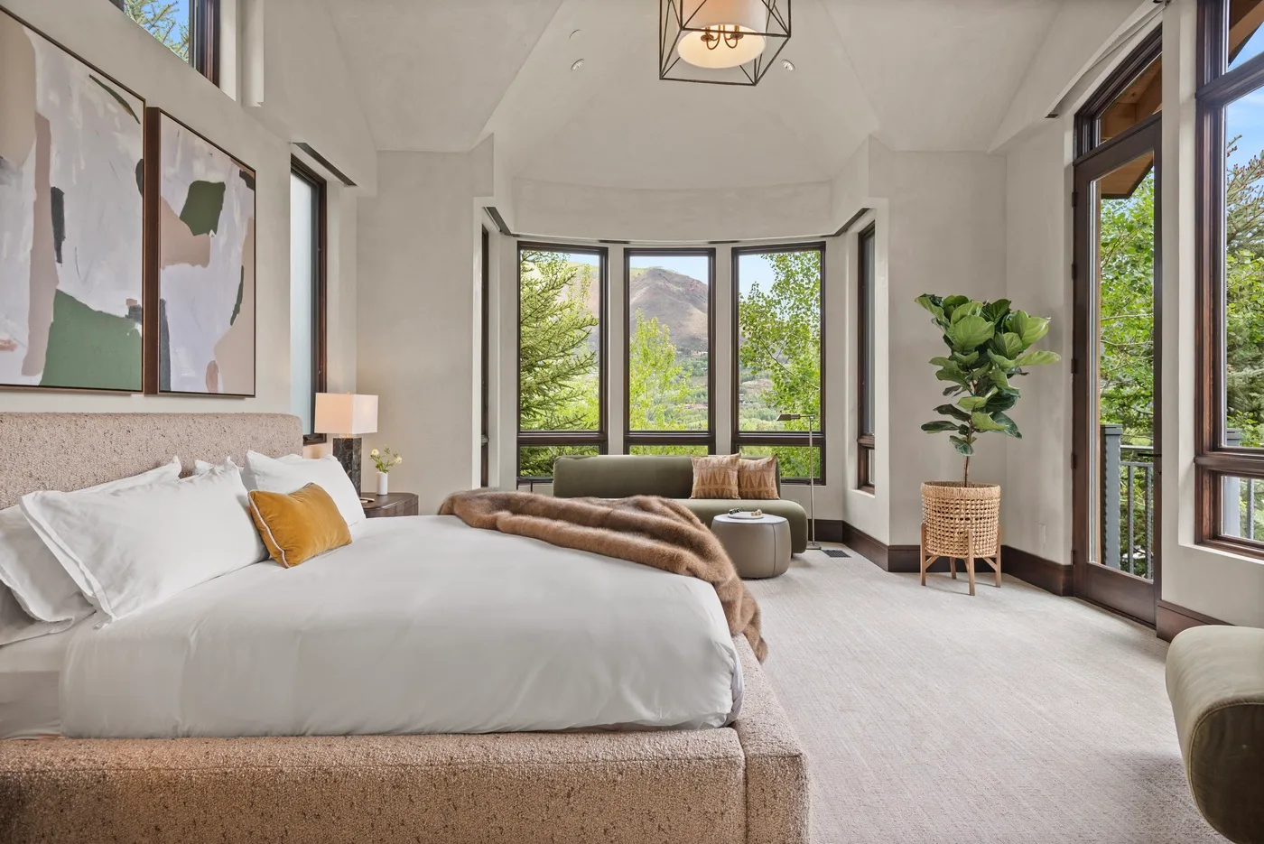 Un dormitorio luminoso con una cama grande, ventanas altas y una planta en maceta.