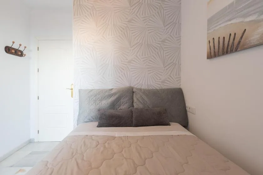 A bedroom with a neatly made bed and patterned wallpaper behind the headboard.
