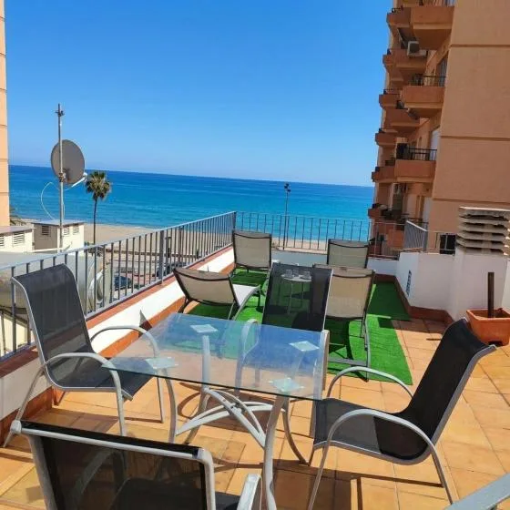A seaside terrace with outdoor seating and a glass table overlooks the blue water.