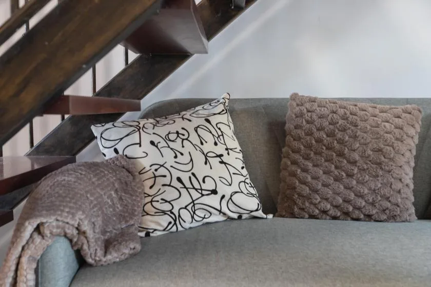 A seating area beneath a staircase has patterned and textured cushions.