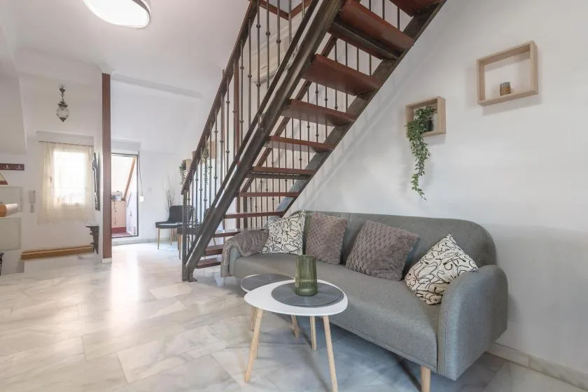 A living room with a gray sofa beneath an open staircase.