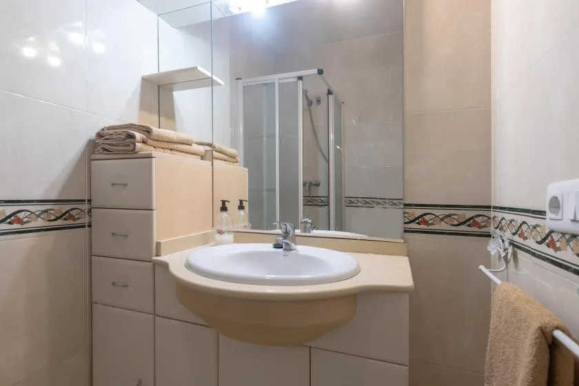 A bathroom with a sink and mirror beside a glass shower.