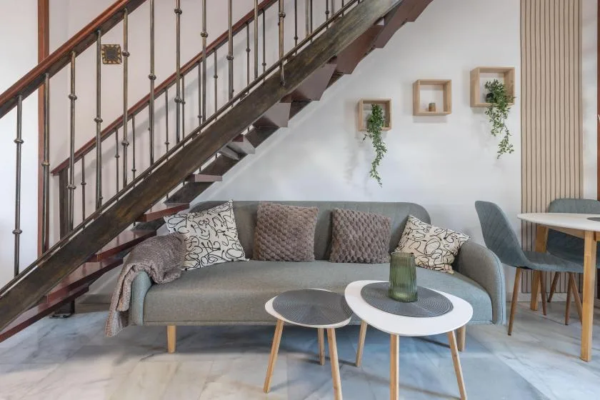 A living room with seating beneath a staircase and two small round tables.