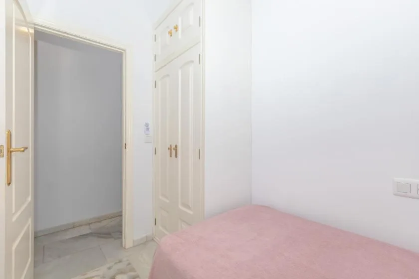A bedroom with a bed covered in pink bedding beside white doors.