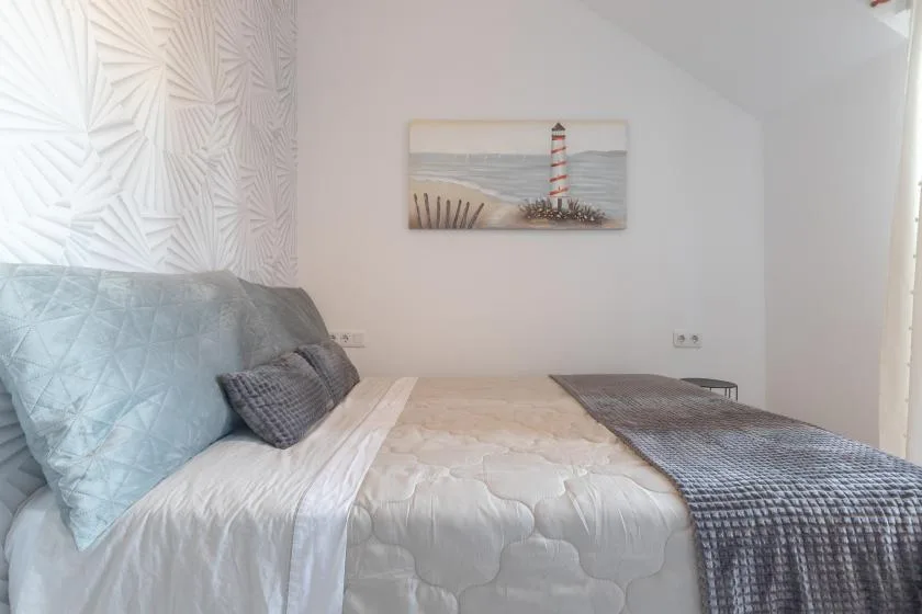 A bedroom with a bed dressed in white bedding and a gray throw.