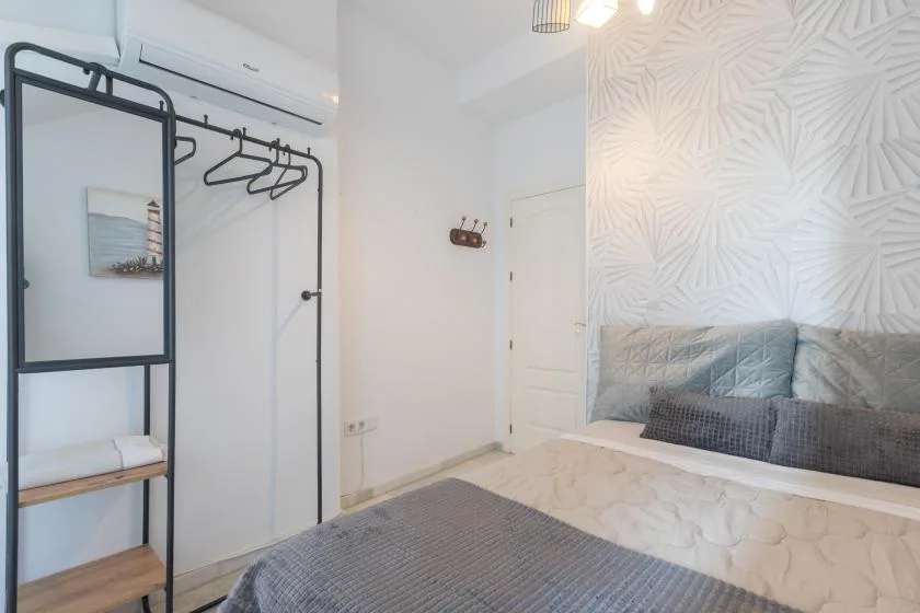 A bedroom with a bed, patterned accent wall, and open clothes rack.