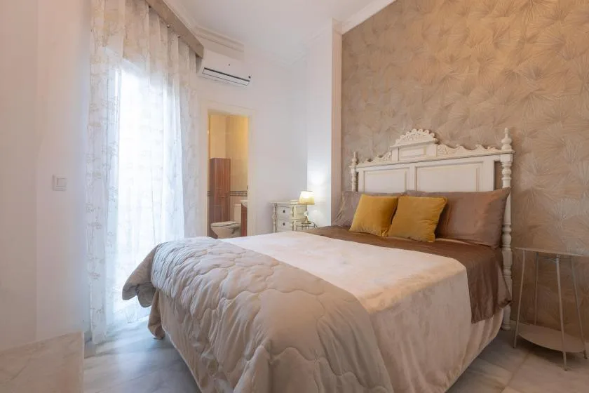 A bedroom with a large bed, bedside table, and sheer curtains.
