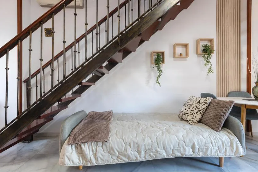 A bedroom with a bed beneath a dark wooden staircase.