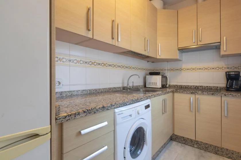 A compact kitchen with light wood cabinets, a countertop, and a washing machine.