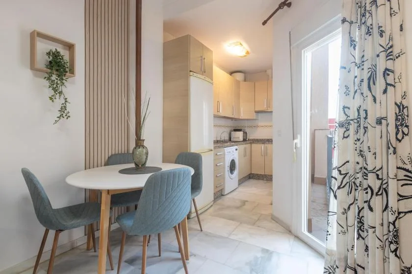 A dining area beside a compact kitchen, with a round table and upholstered seating.