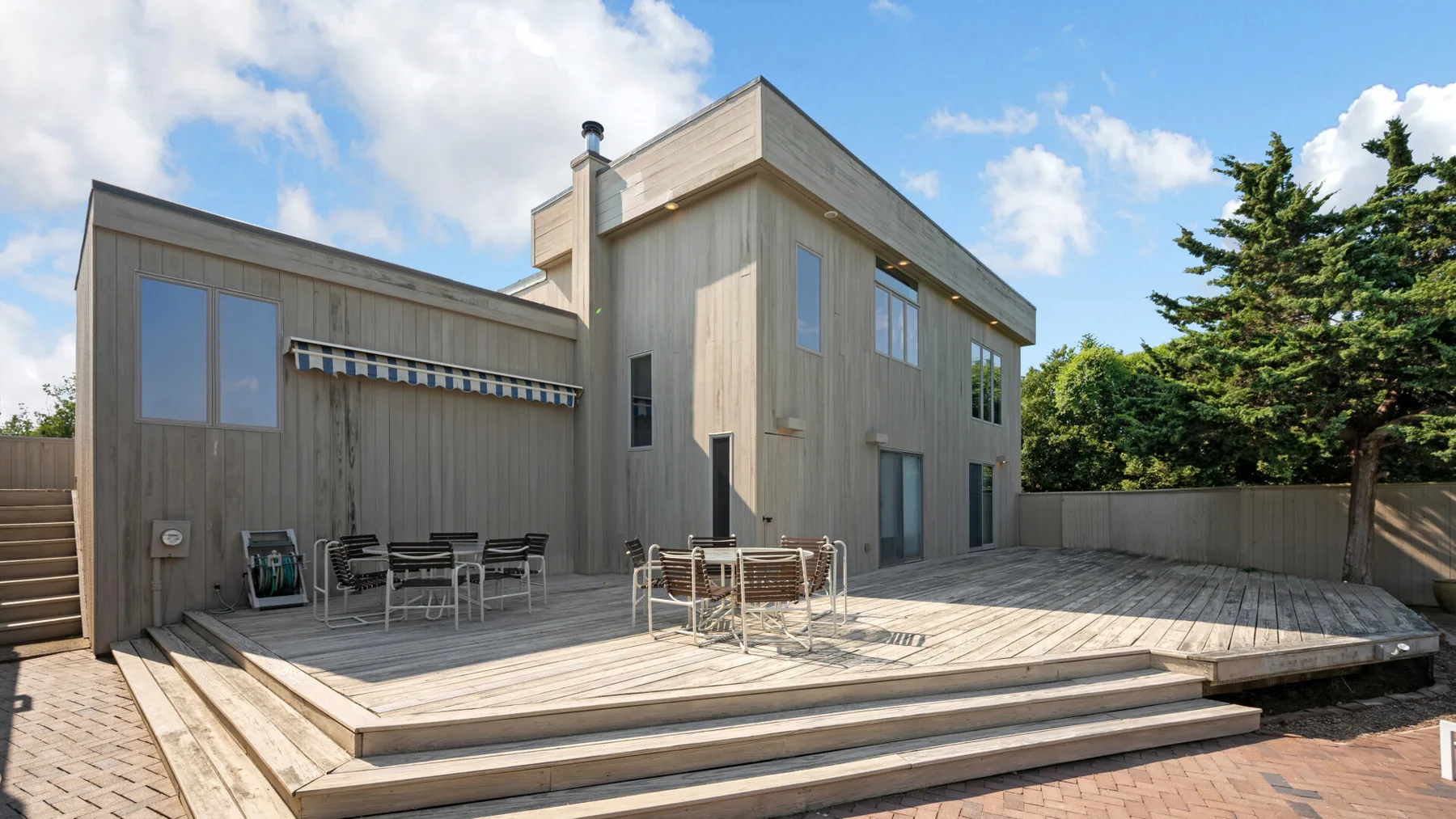 A modern house opens onto a broad wooden deck with outdoor seating.