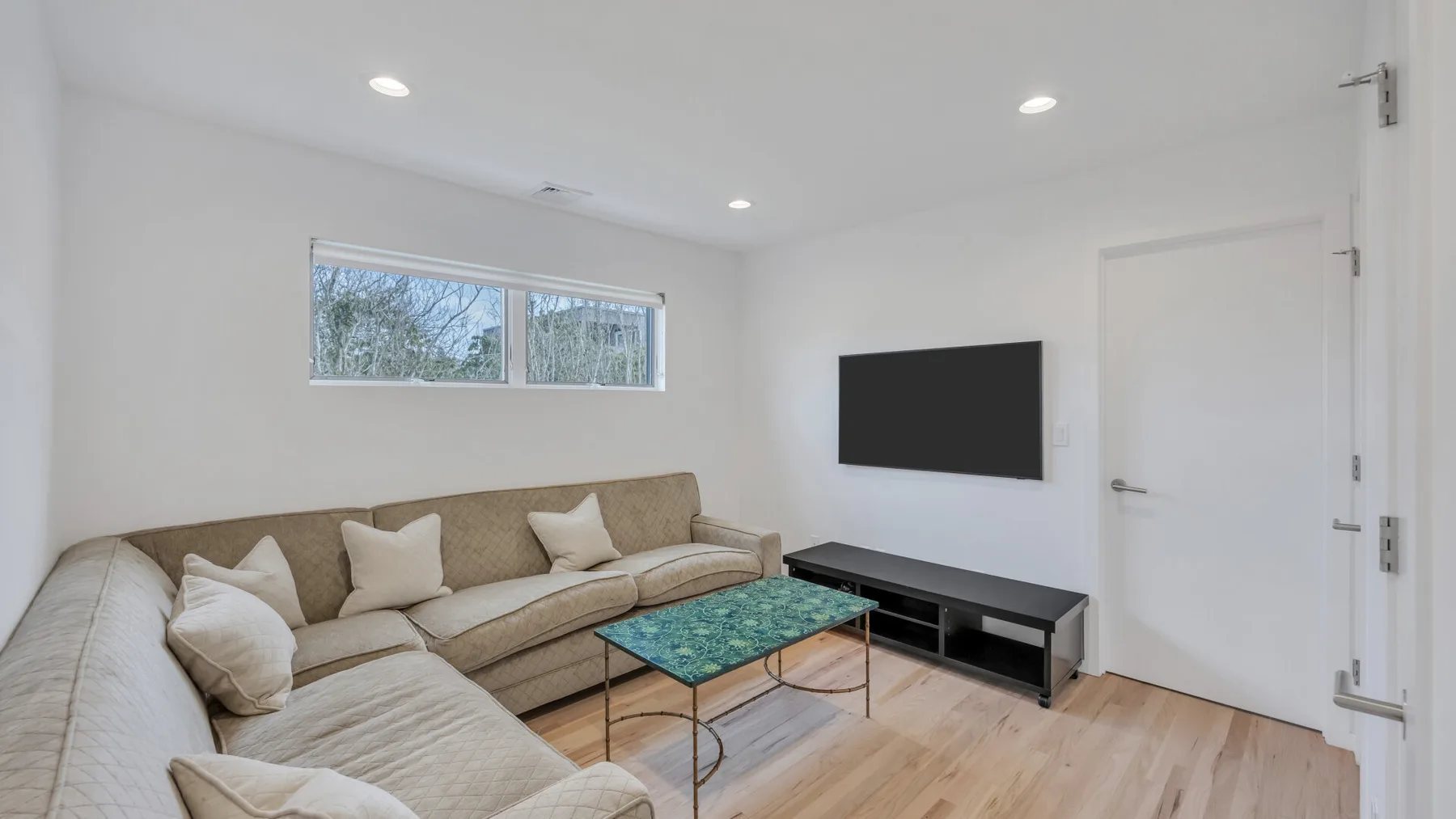 A bright living room with seating, a coffee table, and a wall-mounted television.