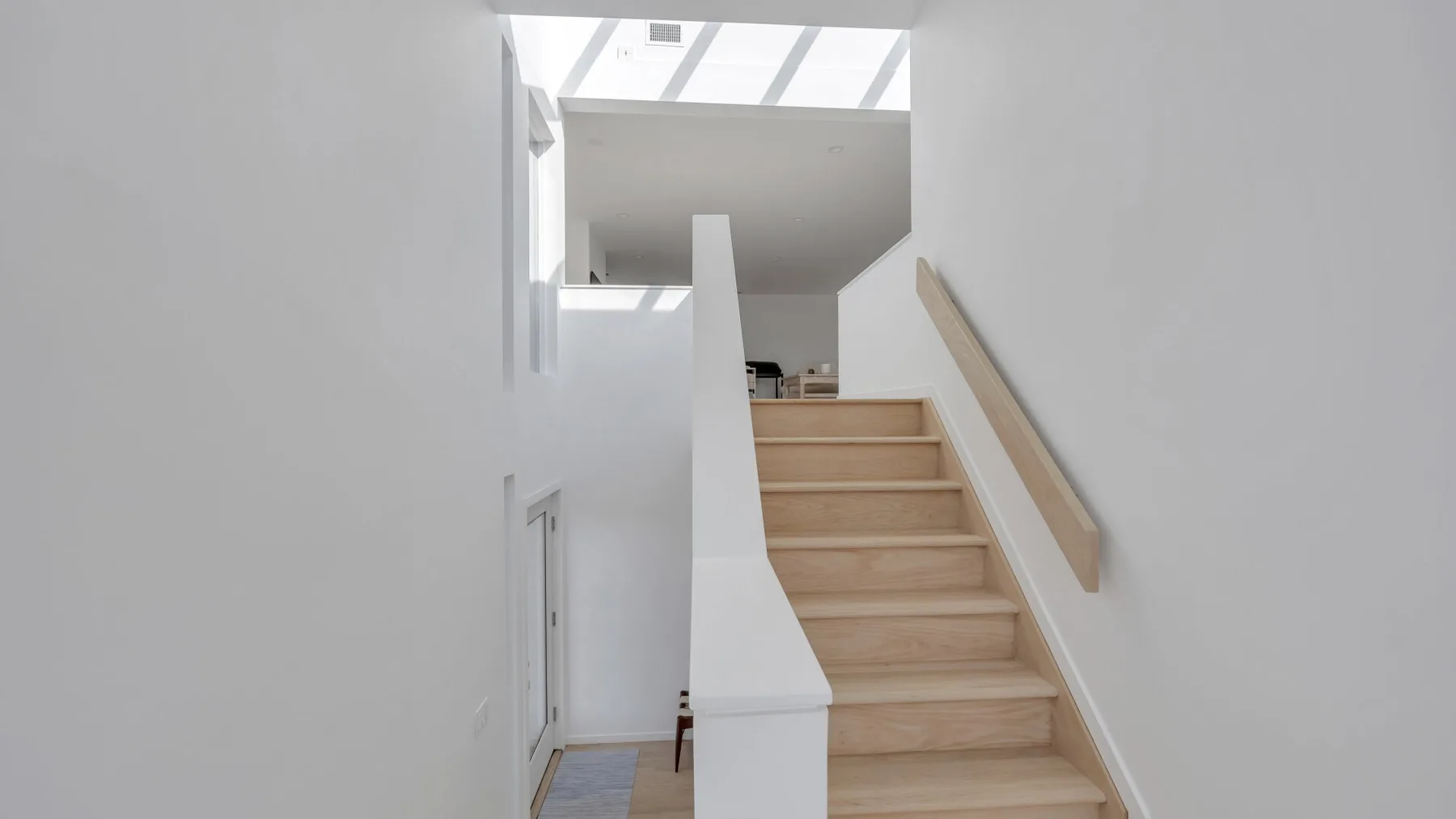 A bright interior staircase with light wood steps and white walls.