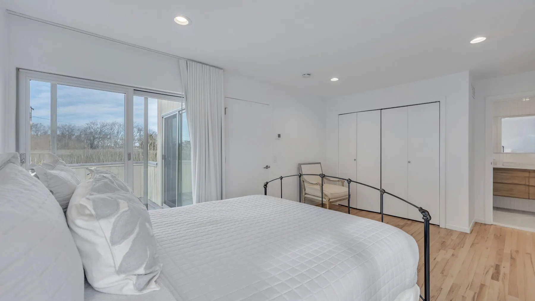 A bright bedroom with a large bed beside a glass door opening to a balcony.