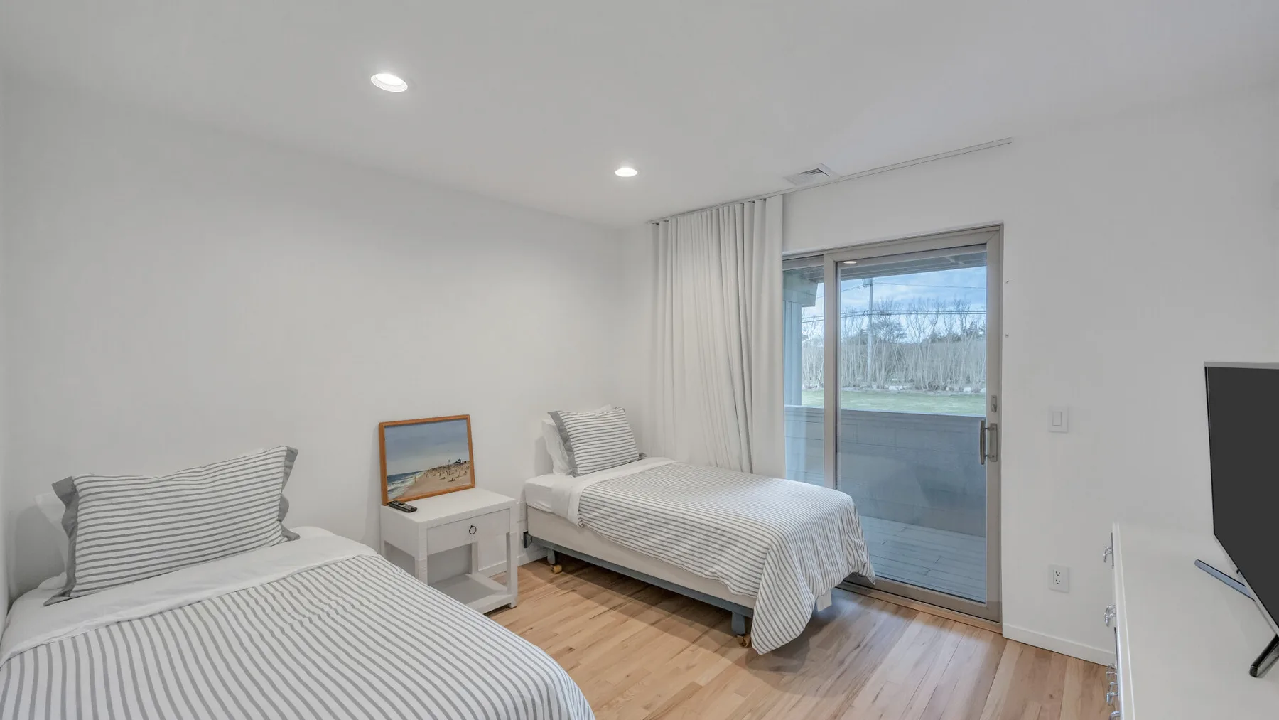 A bright bedroom with two single beds and a sliding glass door.