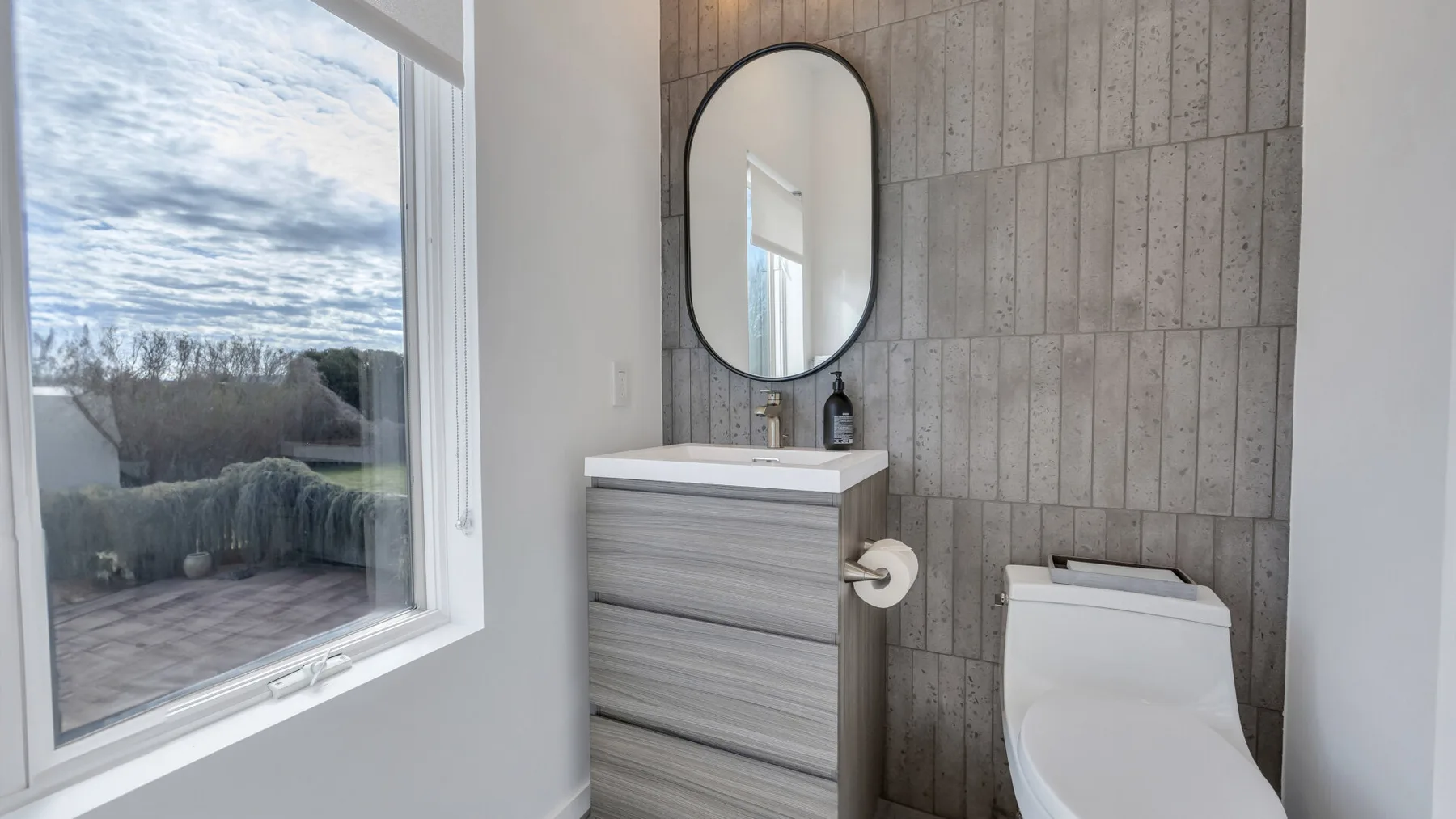 A bathroom with a vanity, mirror, and toilet beside a large window.