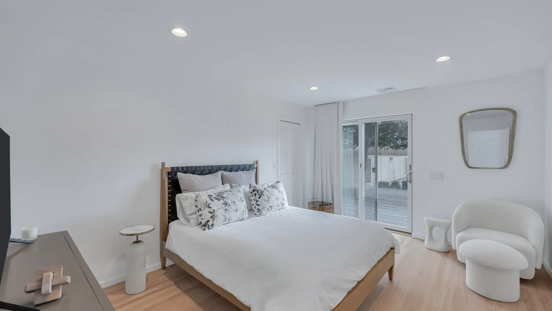 A bright bedroom with a bed, a white armchair, and sliding glass doors.