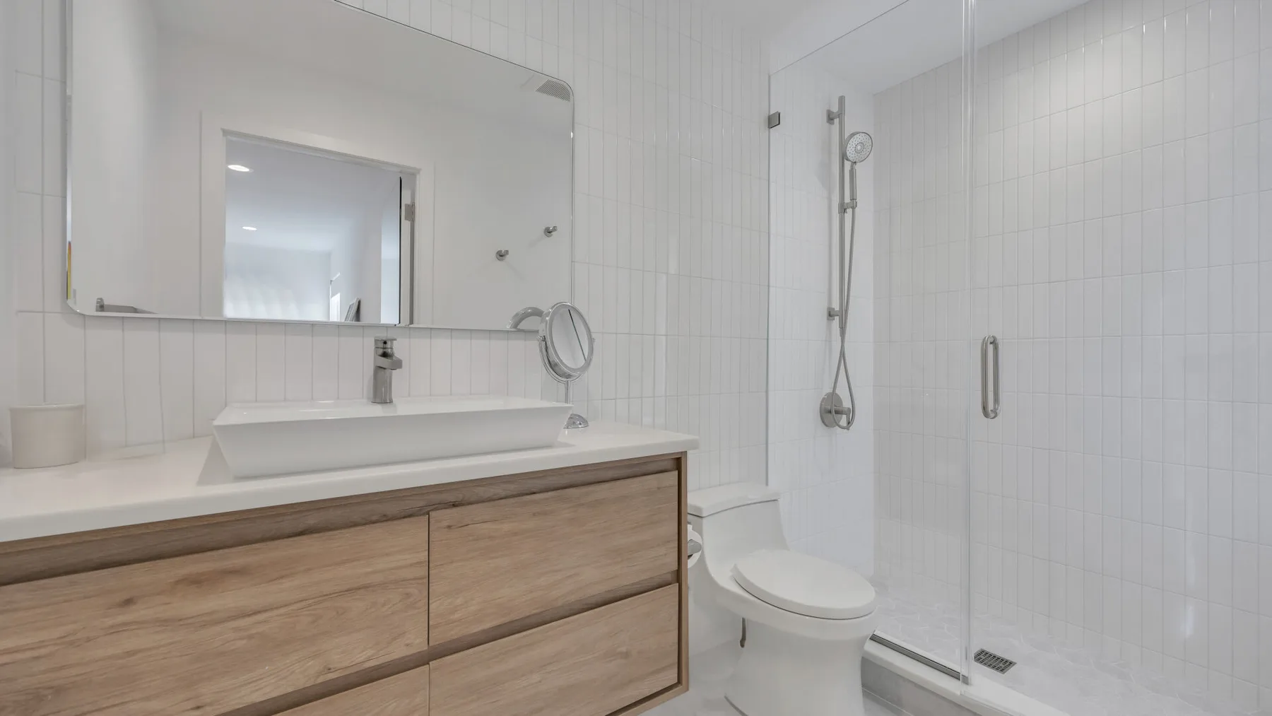 A bright bathroom with a vanity, mirror, toilet, and shower.
