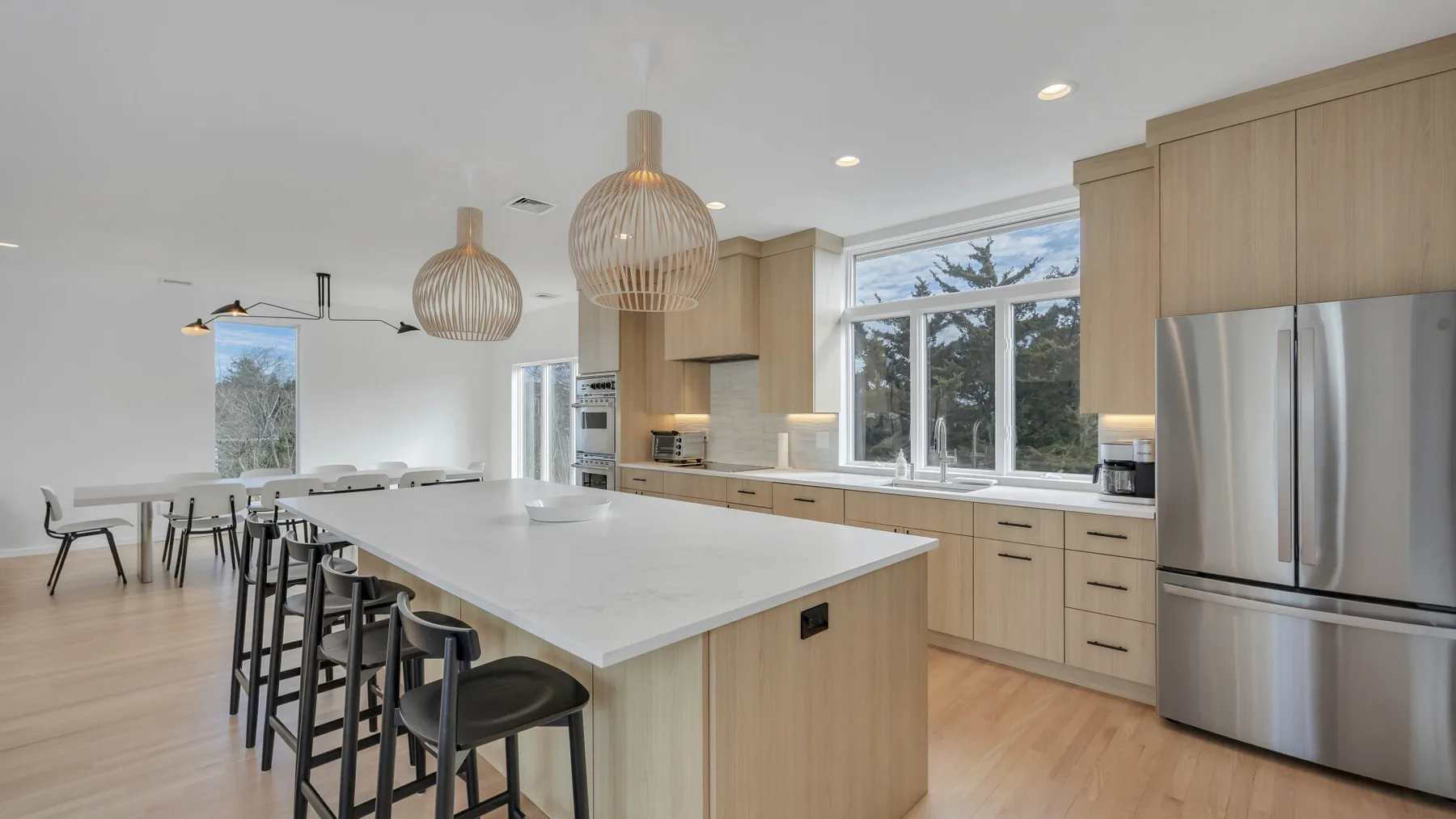 Una cocina luminosa con una isla grande, asientos altos y gabinetes de madera clara.