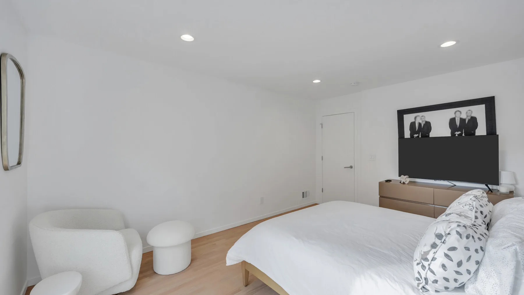A bright bedroom with a bed, a white chair, and a wall-mounted television.