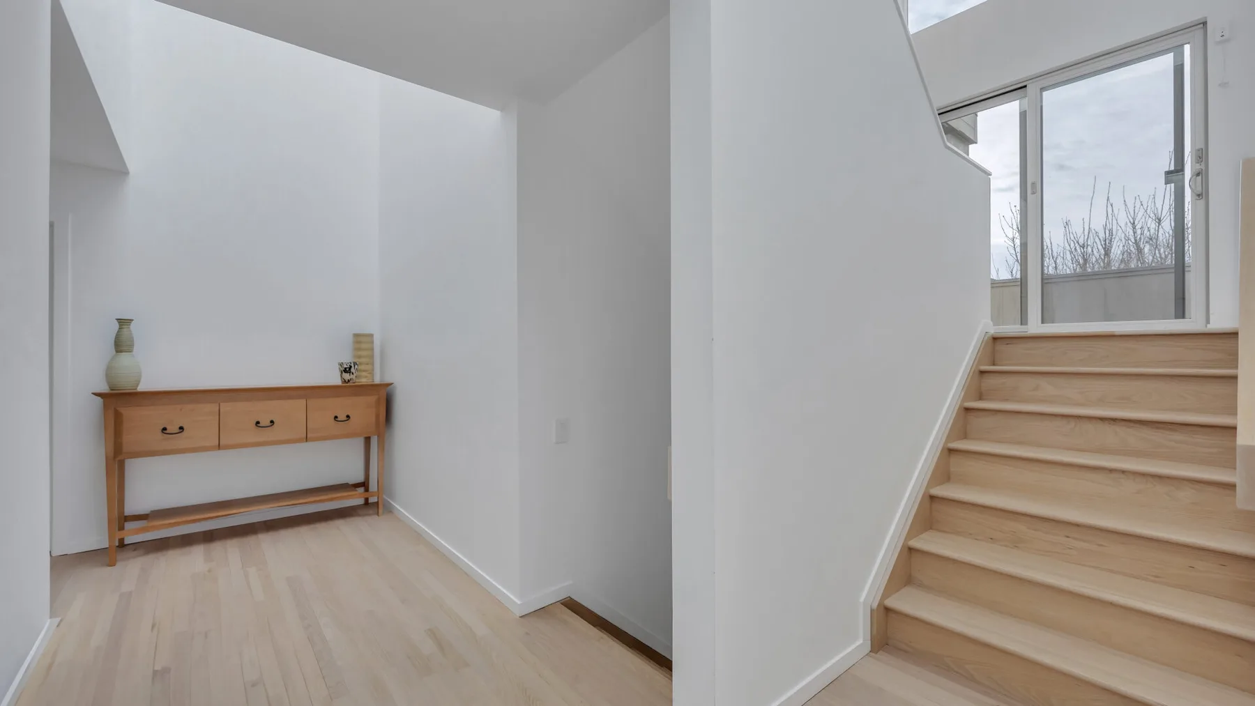 A bright interior entryway with a wooden console beside a staircase.
