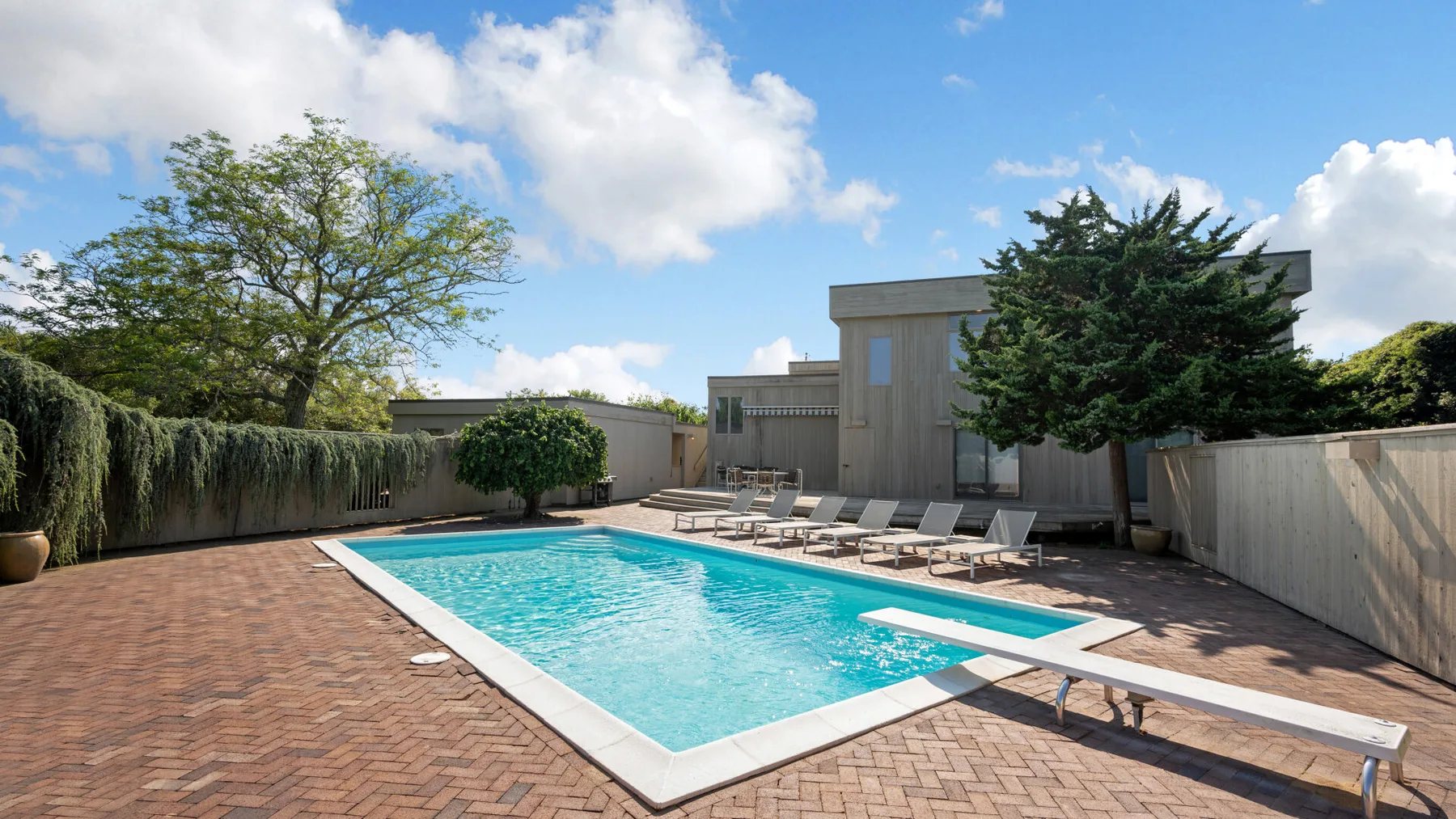 An outdoor swimming pool sits beside a paved deck and lounge chairs.