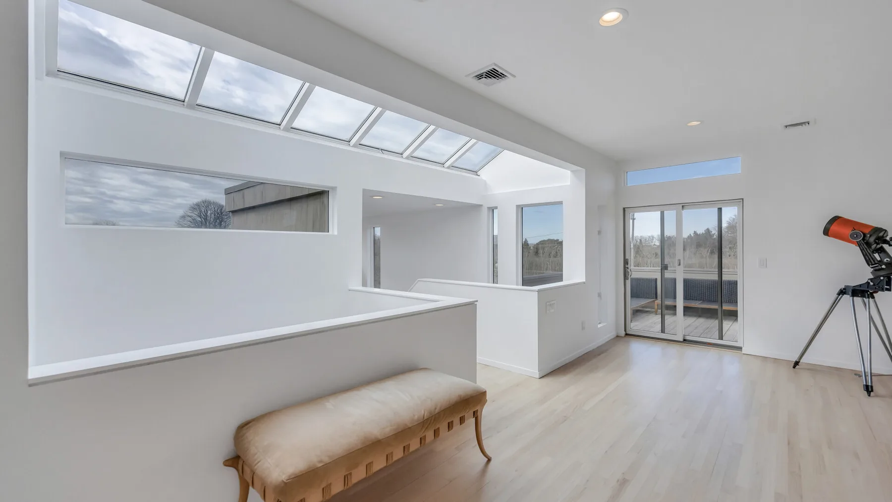 A bright modern interior with slanted skylights, a bench, and sliding glass doors.