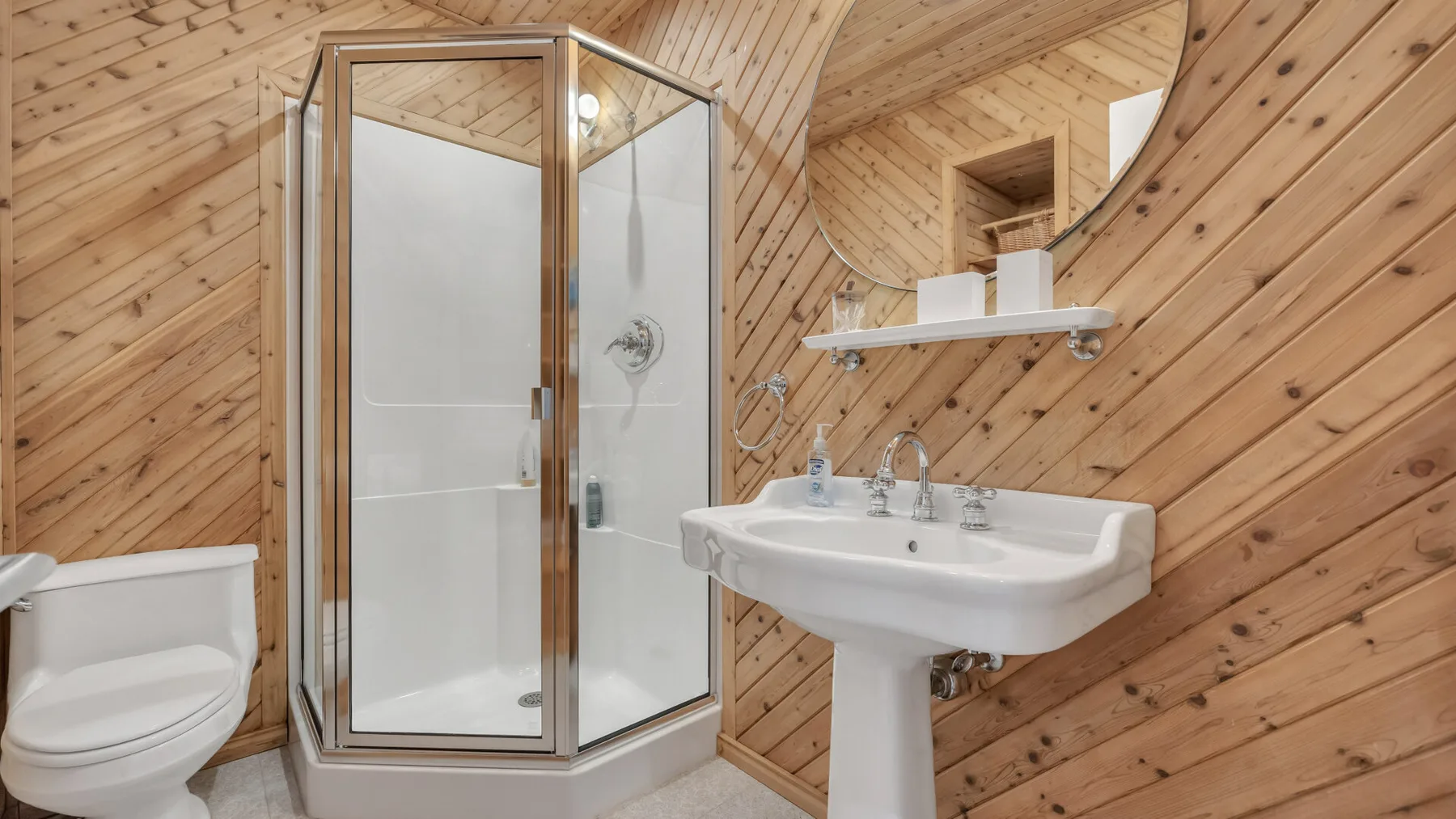 A bathroom with a glass shower, sink, and wood-paneled walls.
