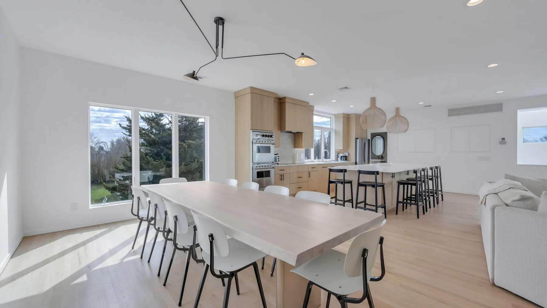 A bright open-plan kitchen and dining area with a long table and bar seating.