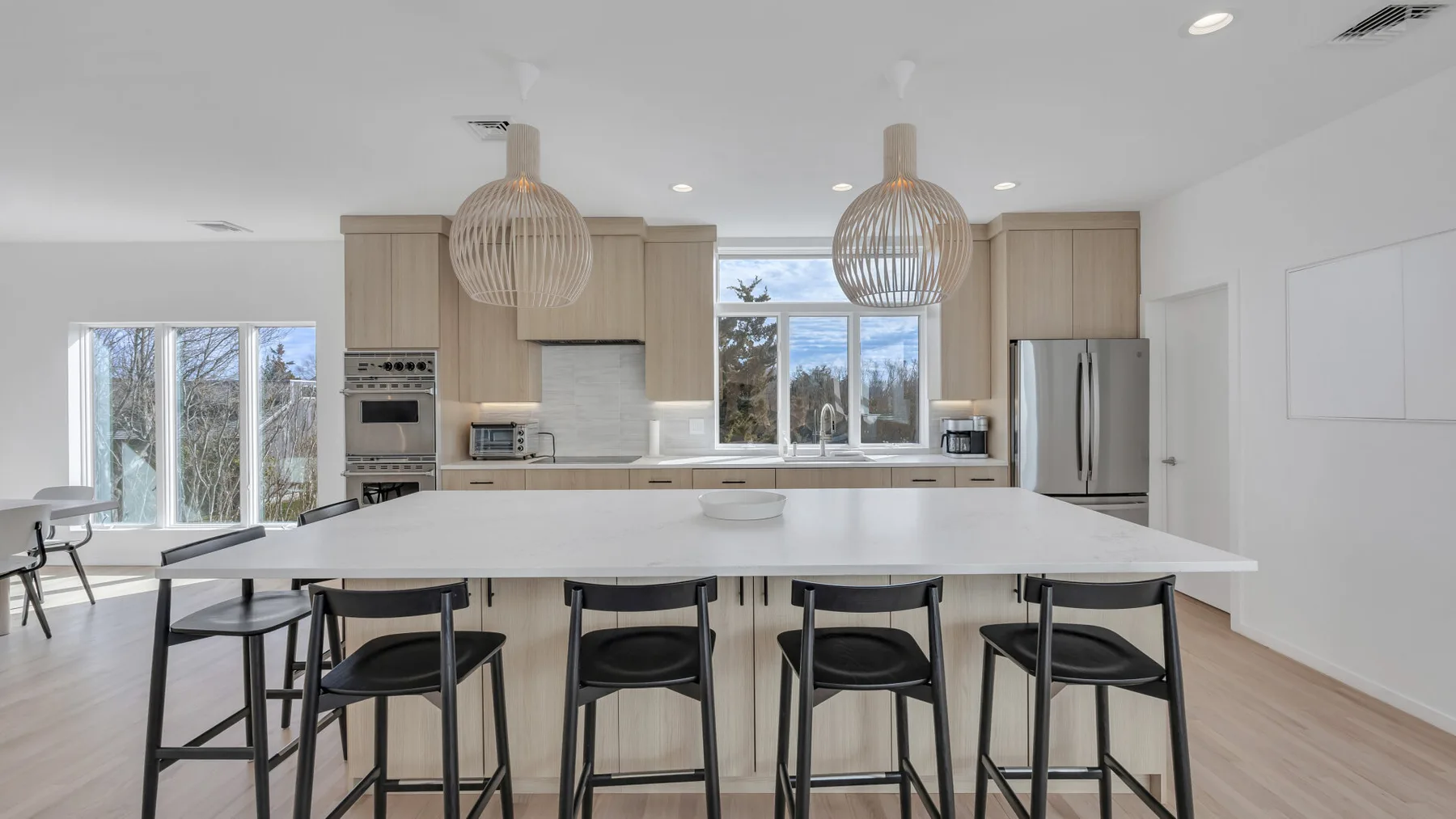 A bright open kitchen has a large island with seating and windows overlooking trees.