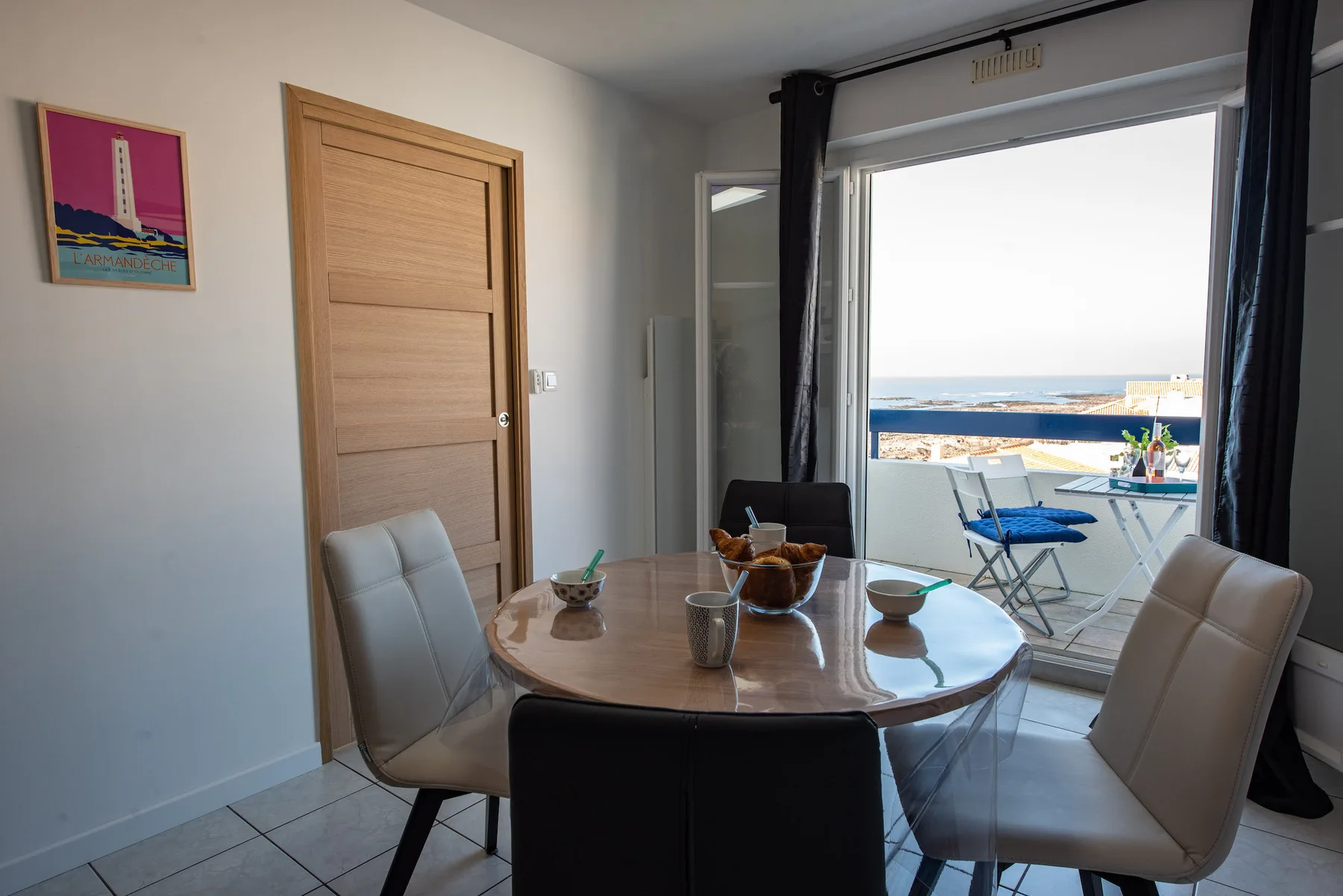 Dining area with a table and seating beside a balcony overlooking the sea.