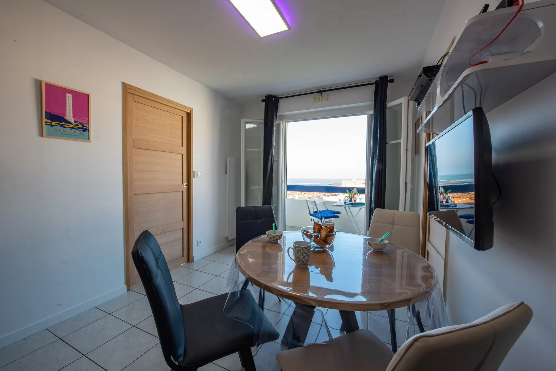 Dining area with seating around a table beside a large window.