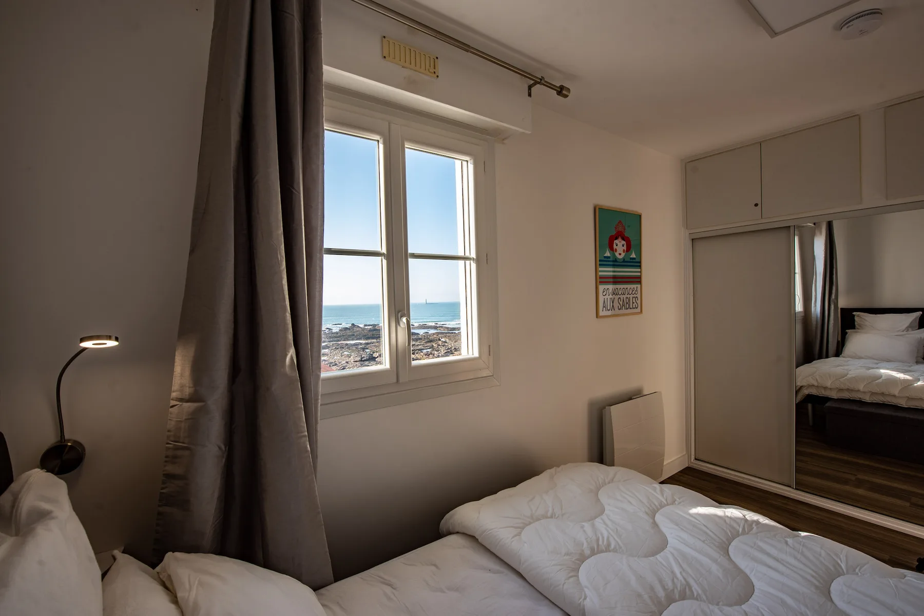 A bedroom with a bed beside a window overlooking the sea.
