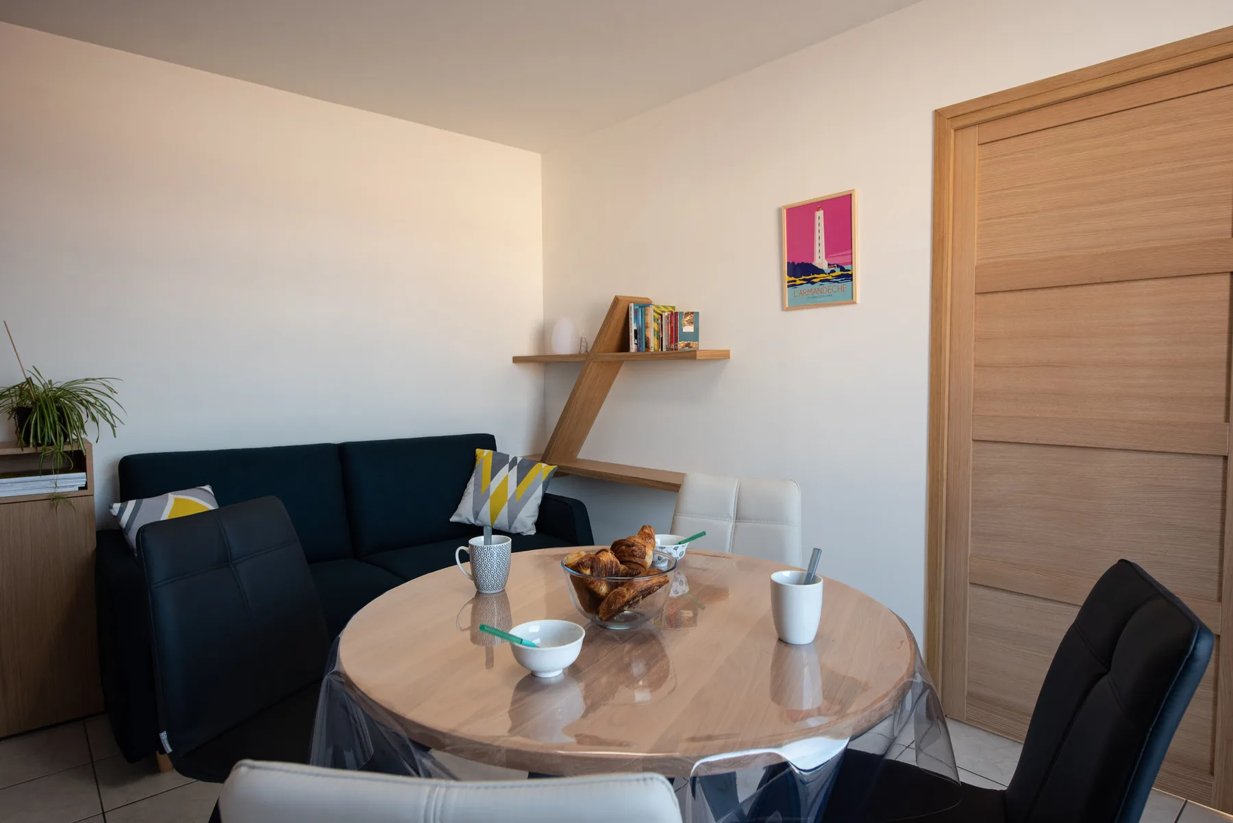 A dining area with a round table, dark seating, and wall shelves.