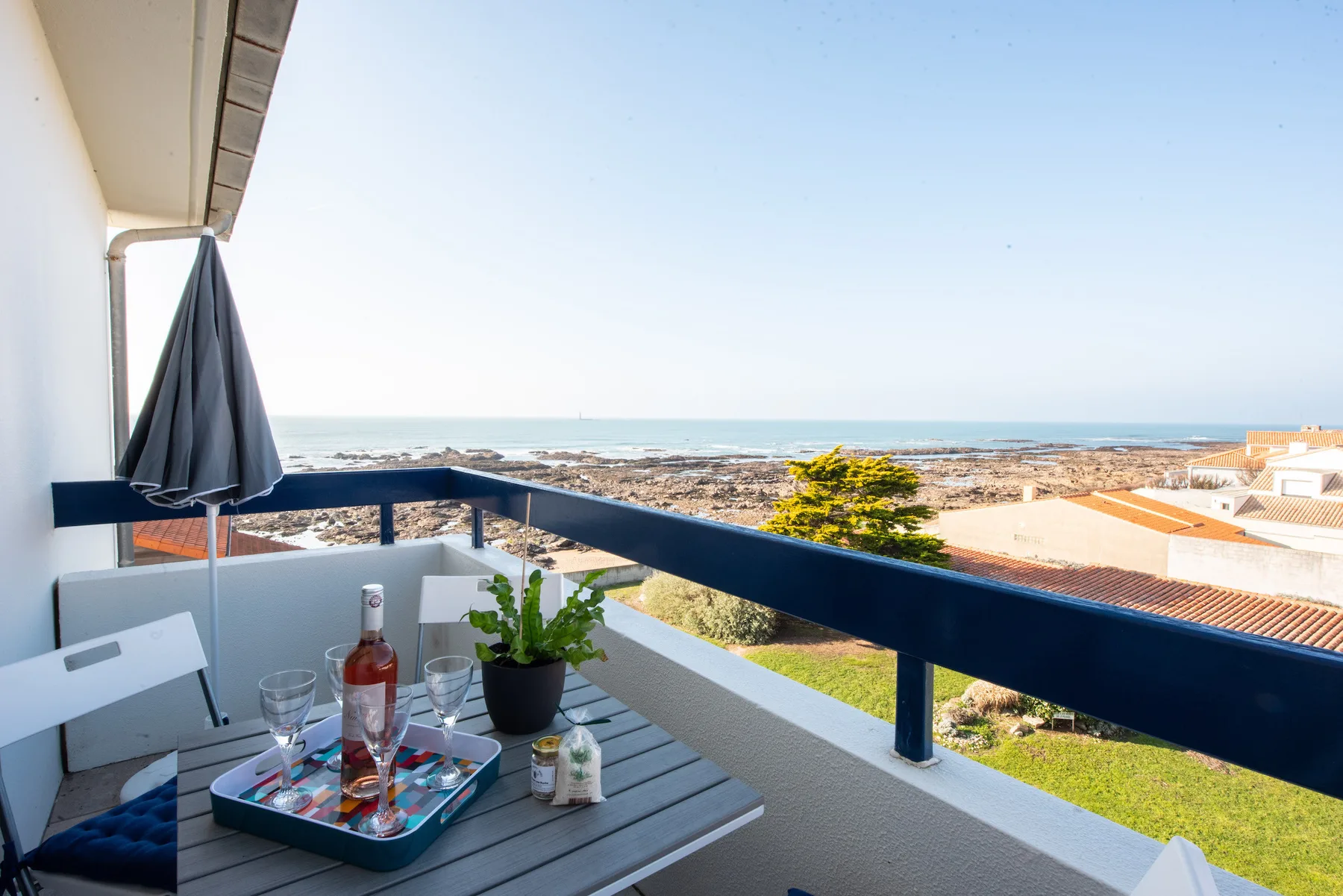 A balcony dining area overlooks the coastline, with a table and closed umbrella.