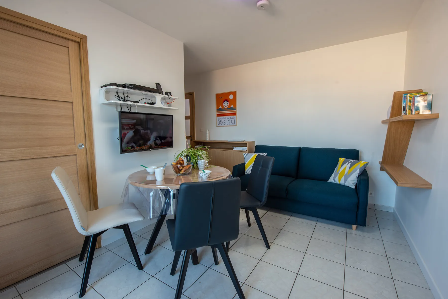 A living and dining area with a teal sofa and a table surrounded by chairs.