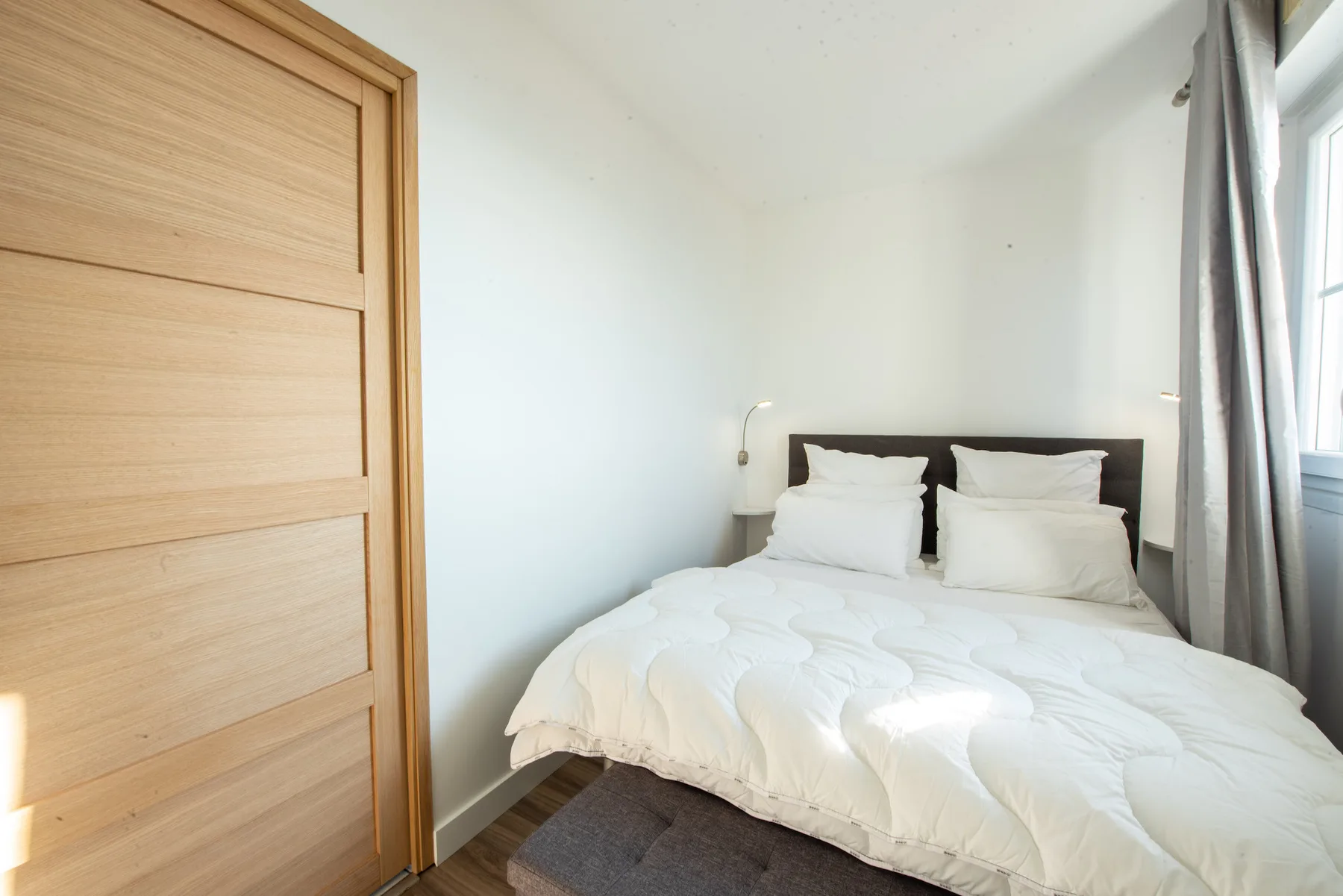 A bright bedroom with a bed dressed in white bedding.