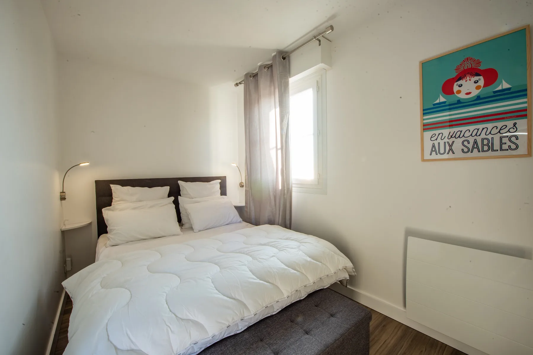 A bright bedroom with a bed beside a sunlit window.
