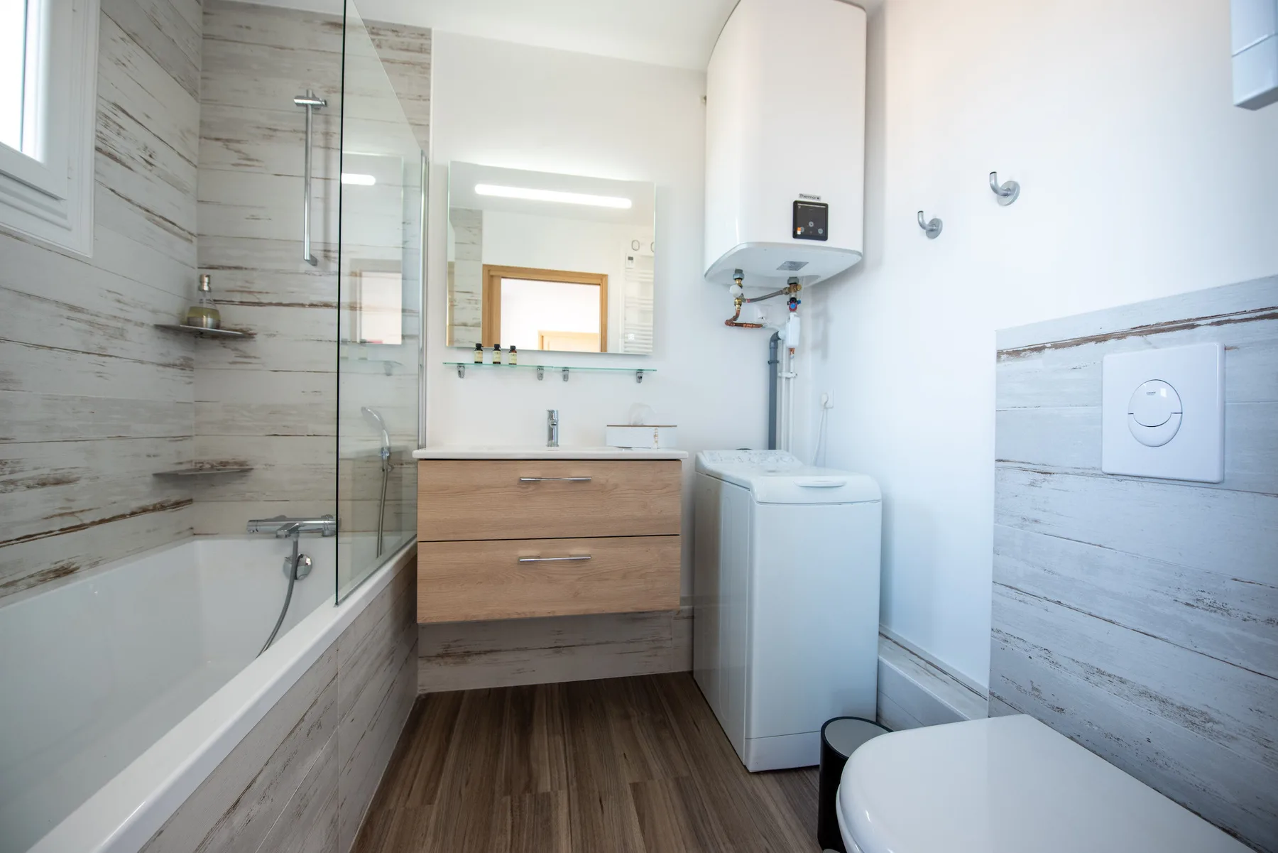 A bright bathroom with a bathtub, sink, washing machine, and toilet.