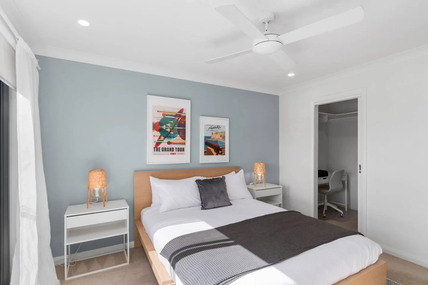 Un dormitorio con la cama tendida y un escritorio visible a través de la puerta abierta.