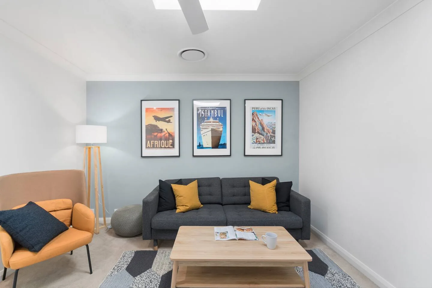 Una sala de estar con un sofá gris, un sillón naranja y cuadros enmarcados.