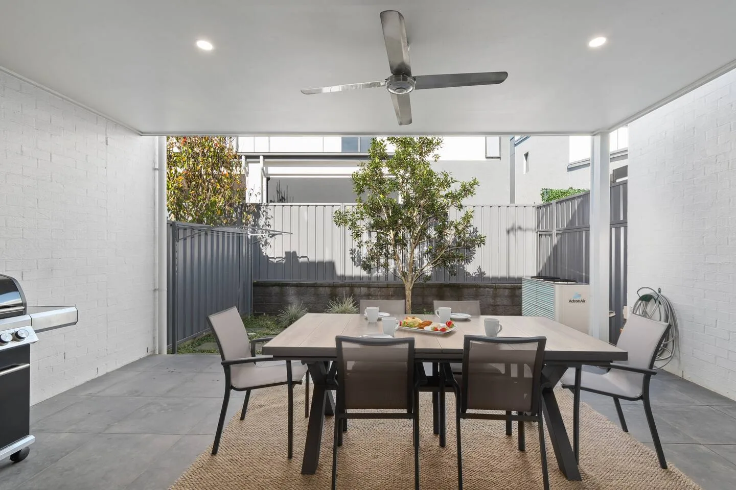 Una zona de comedor exterior cubierta con una mesa y asientos junto a un árbol pequeño.