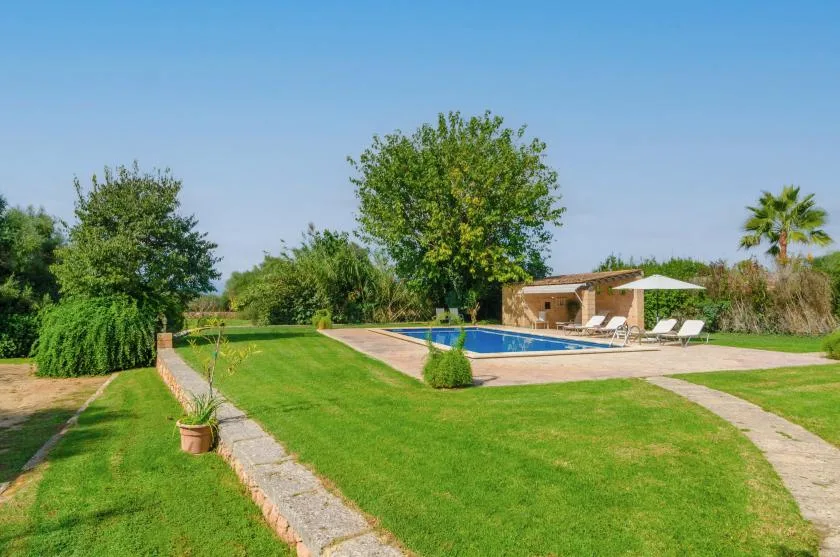 Una piscina al aire libre está junto a un amplio césped verde y árboles frondosos.