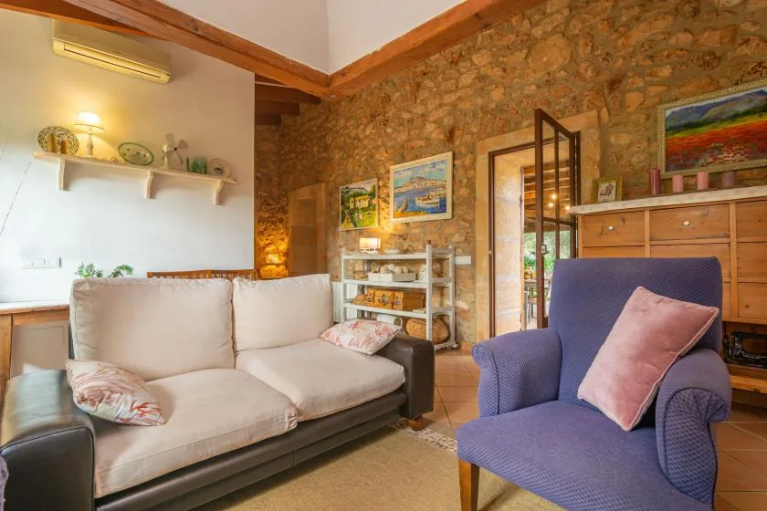 Una sala de estar con asientos claros, un sillón azul y paredes de piedra.