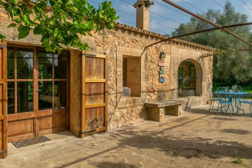 Un patio de piedra con puertas de madera, un banco y asientos al aire libre.