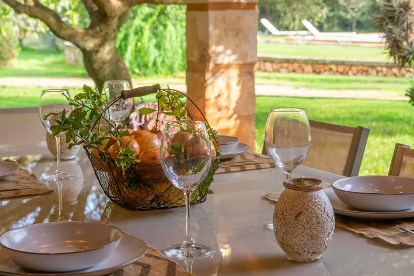 Una mesa puesta con platos, copas y un centro de mesa está en un patio cubierto.