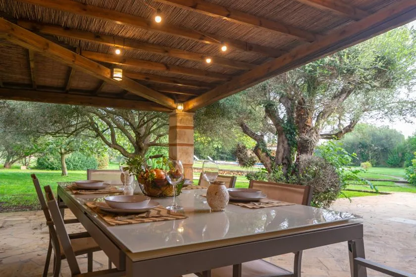 Una zona de comedor exterior cubierta se abre a un jardín frondoso.
