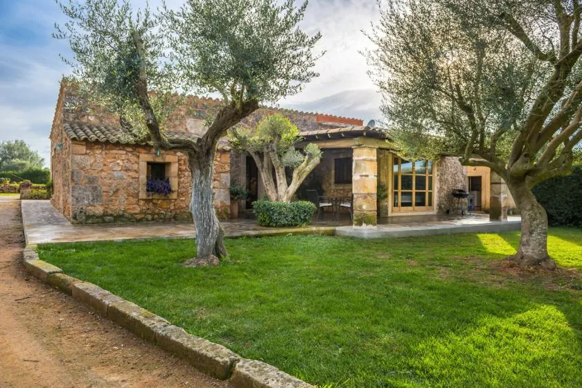 Una casa de piedra se encuentra detrás de un césped y varios árboles.